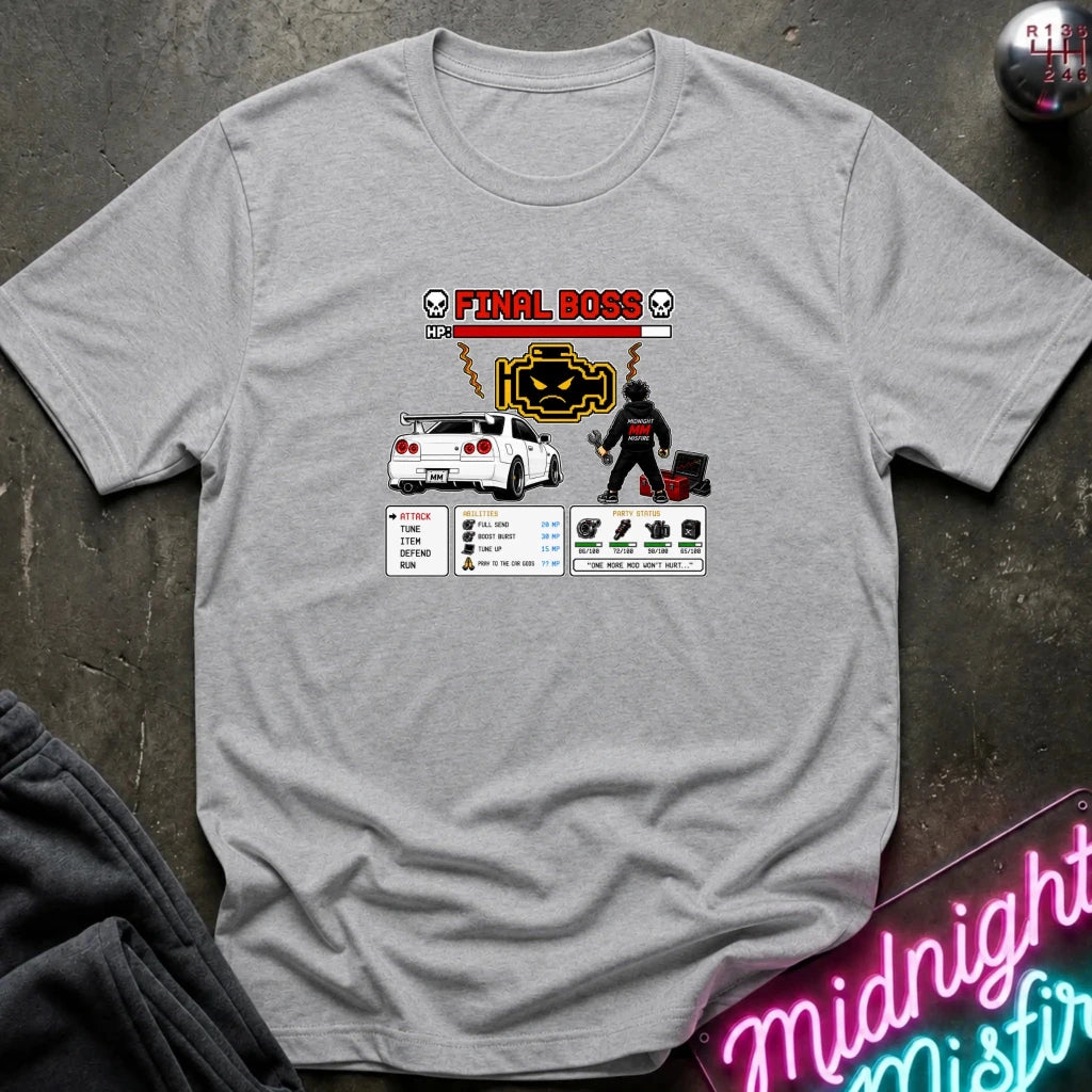 A light gray graphic t-shirt laid flat on a dark textured surface. The shirt features a 'Final Boss' engine design inspired by the rpg game.