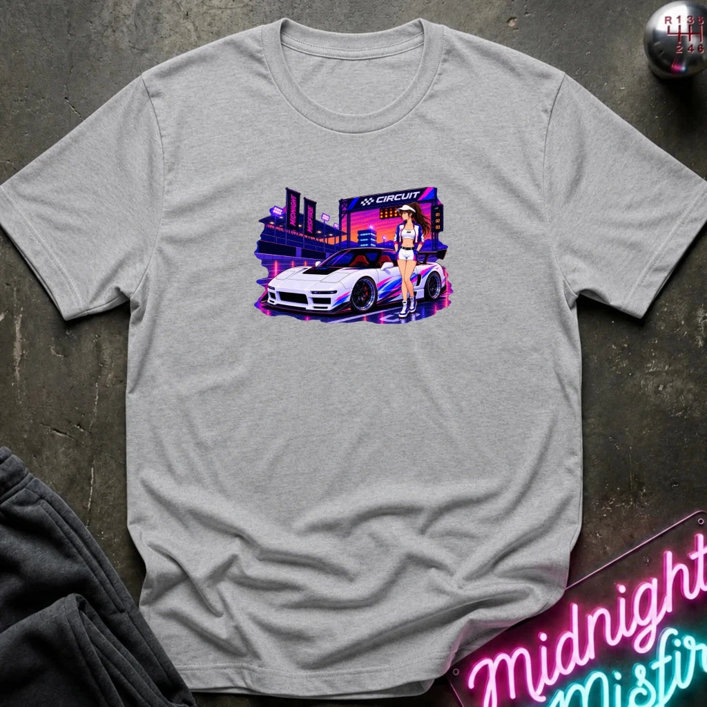 A light heather gray  short-sleeve t-shirt laid flat on a dark textured surface, featuring a colorful graphic print of a white sports car and a woman in a neon-lit scene. beside it.