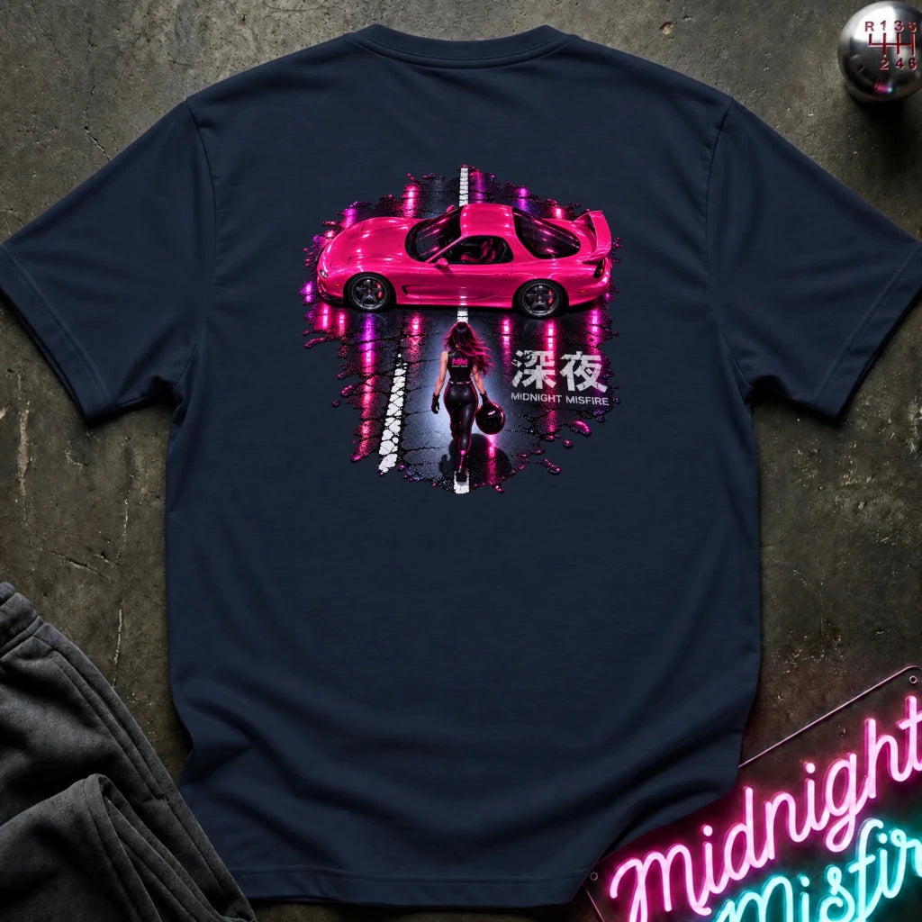 A navy blue t-shirt laid flat on a dark textured surface, featuring a large graphic print on the back with a pink sports car, a woman walking, Japanese characters