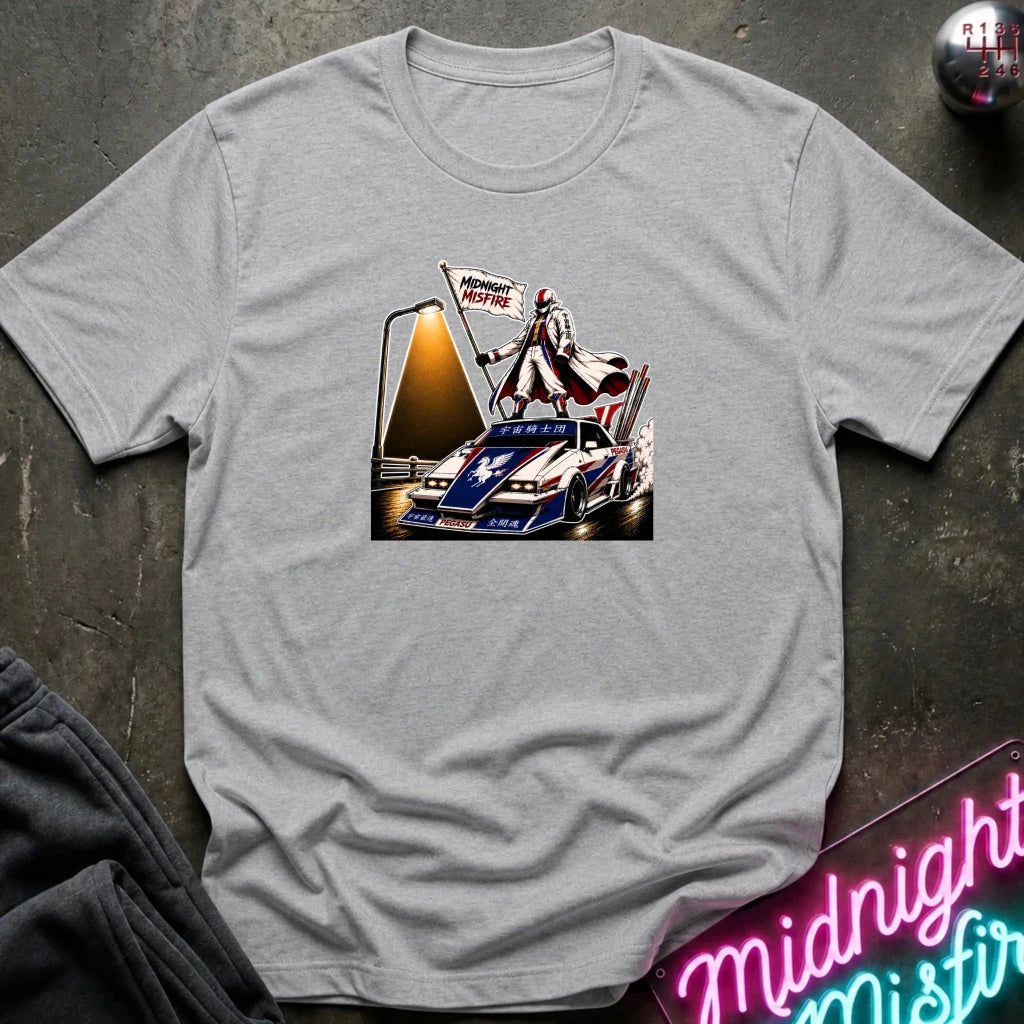 A light gray heather short-sleeve t-shirt laid flat on a dark textured surface, featuring a detailed graphic print of a vintage race car with a driver and a 'Midnite Misfire' flag. 