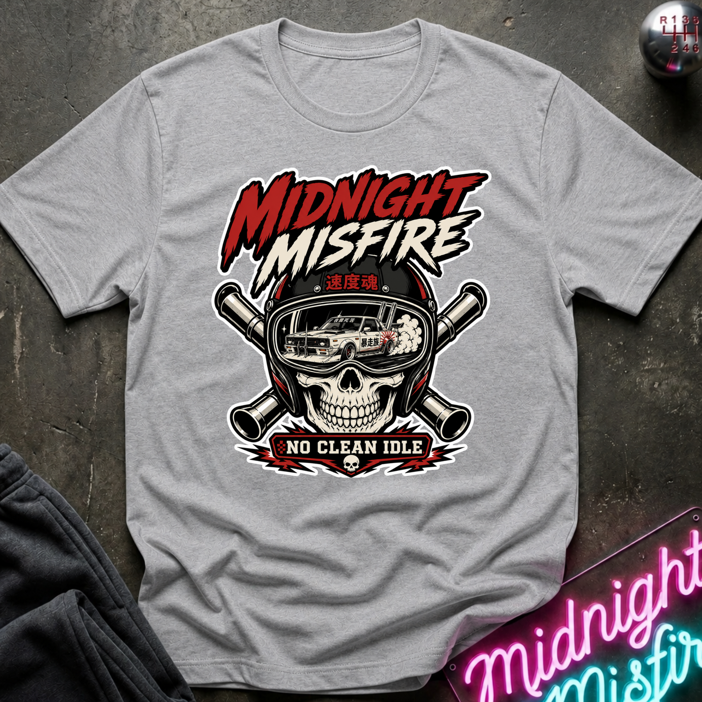 A light gray crewneck t-shirt featuring a bold graphic print of a skull in a racing helmet with crossed bats behind it. The text 'MIDNIGHT MISFIRE' is printed in a red and white stylized font above the helmet, and 'NO CLEAN IDLE' is printed below it.