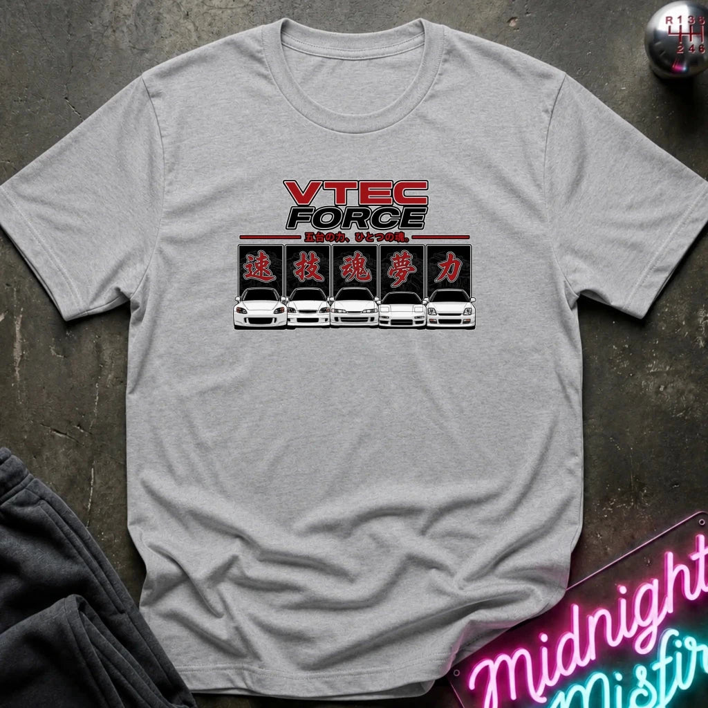 A light gray crewneck t-shirt featuring a 'VTEC FORCE' graphic with red and black lettering, Japanese katakana characters, and a row of white sports cars. The shirt is laid flat on a dark textured surface with a neon sign and dark pants partially visible.