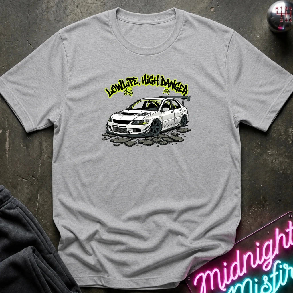 A light gray heather crewneck t-shirt featuring a graphic of a white Mitsubishi Lancer Evolution with yellow 'LOWLIFE, HIGH DANGER!' text above it, displayed on a dark textured background with a neon sign and sweatpants.