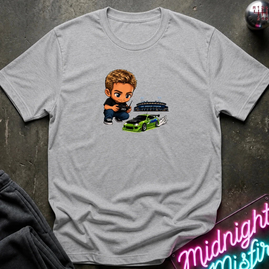 A heather gray graphic t-shirt laid flat on a dark textured surface. The graphic features a green car, and person  controlling it with remote.