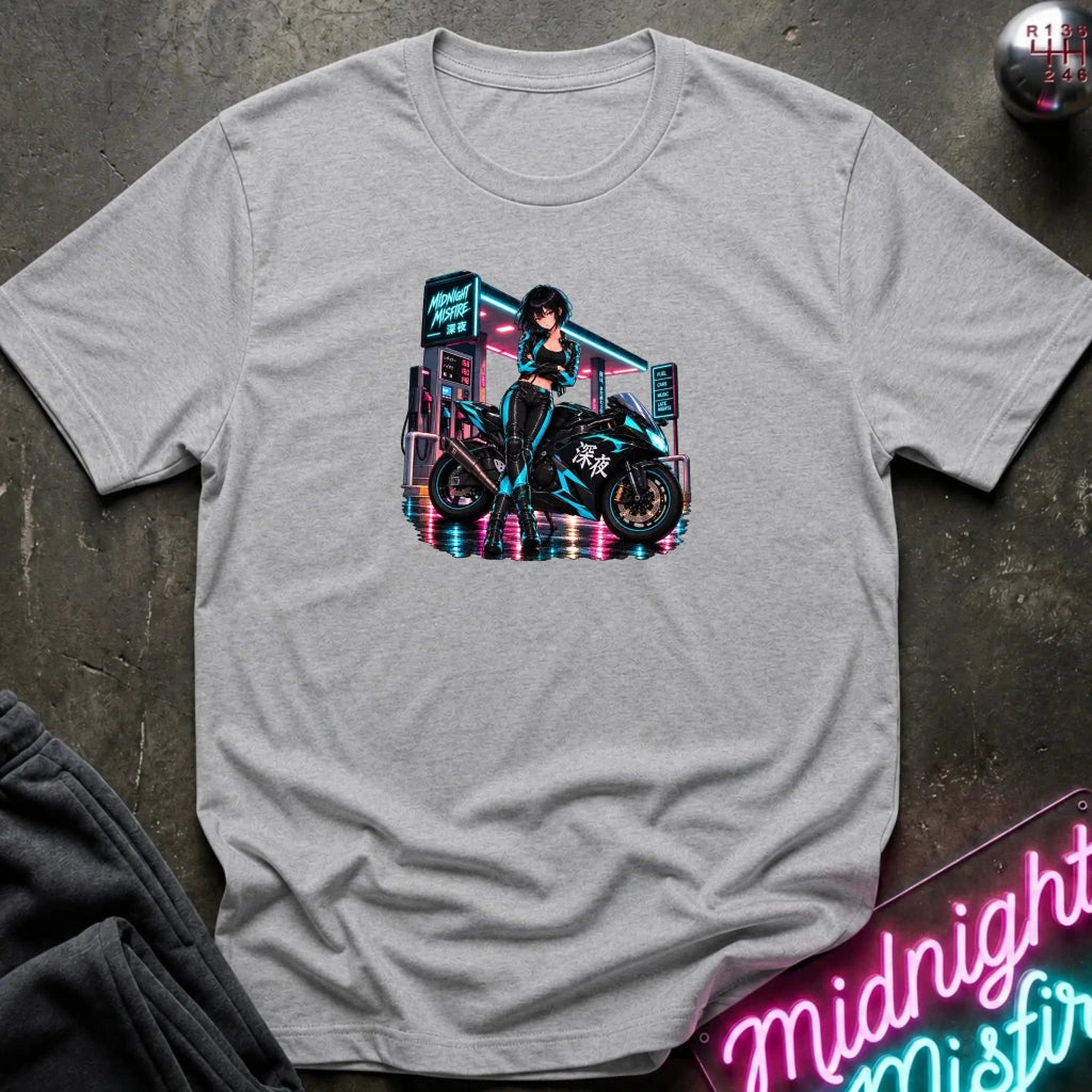 A heather gray short-sleeve t-shirt with a colorful graphic of a woman in a black leather outfit riding a motorcycle in front of a neon sign, displayed on a dark textured background with a neon sign and sweatpants partially visible.