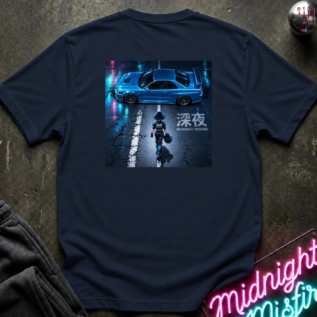 A navy blue short-sleeve t-shirt laid flat on a dark textured surface, featuring a large rectangular graphic print on the back with a blue car, a figure walking on wet pavement, and Japanese text. 