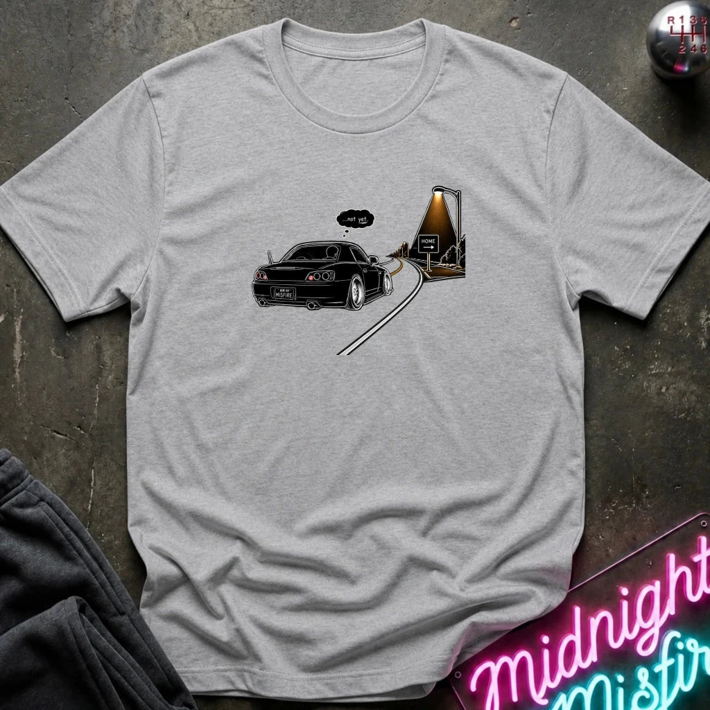 A light heather gray short-sleeve t-shirt laid flat on a dark textured surface, featuring a graphic print of a black sports car driving passed sign that says home.