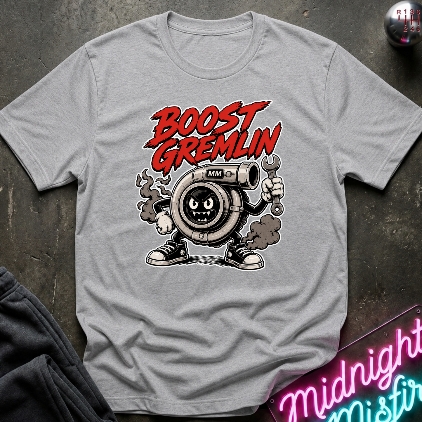 A light gray crewneck t-shirt featuring a cartoon graphic of a turbocharger character with the text 'BOOST GREMLIN' in red, laid flat on a dark textured surface.