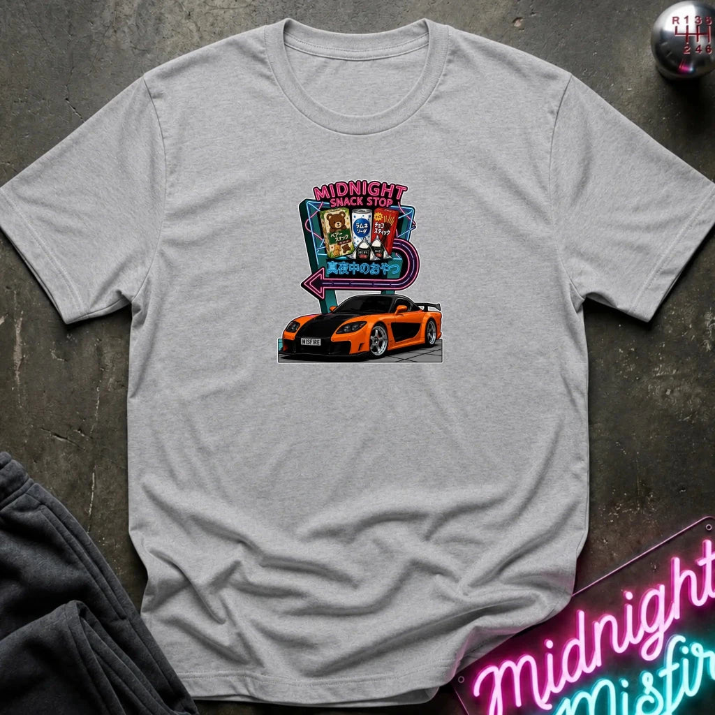 A light gray heather  short-sleeve t-shirt laid flat on a dark textured surface, featuring a colorful graphic print of an orange sports car in front of a neon sign that reads 'Midnight Snack Stop'.