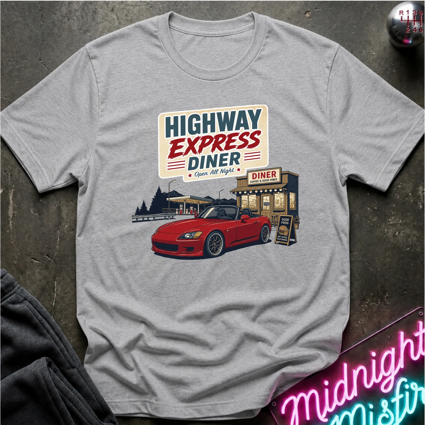 A light gray crewneck t-shirt featuring a retro-style graphic of a red convertible car parked outside a diner with the text 'HIGHWAY EXPRESS DINER' on the front, laid flat on a dark textured surface.