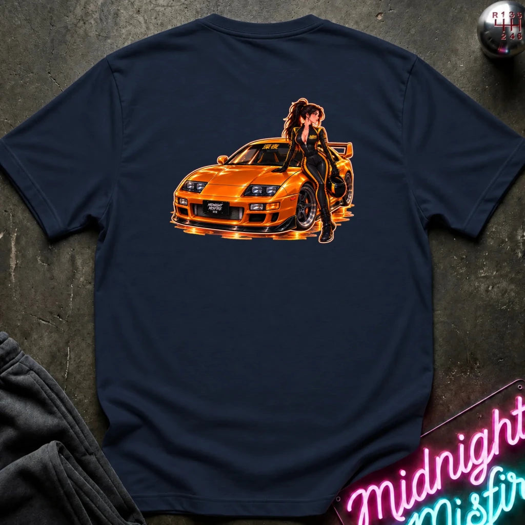 A navy blue short-sleeve t-shirt laid flat on a dark textured surface, featuring a large graphic print on the back of an orange sports car with a woman in a black racing suit. 