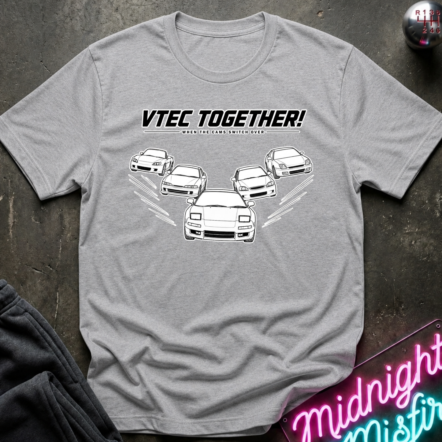 A heather gray short-sleeve t-shirt with a white graphic print of five cars and the text 'VTEC TOGETHER!' laid flat on a dark textured surface.
