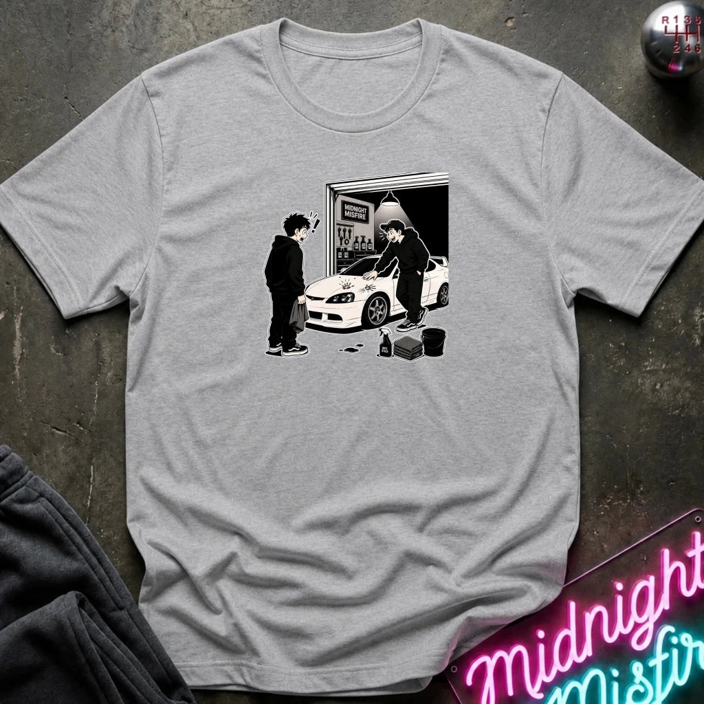 A light gray crewneck t-shirt with a black and white graphic print of a person standing next to a white sports car in front of a garage door. 