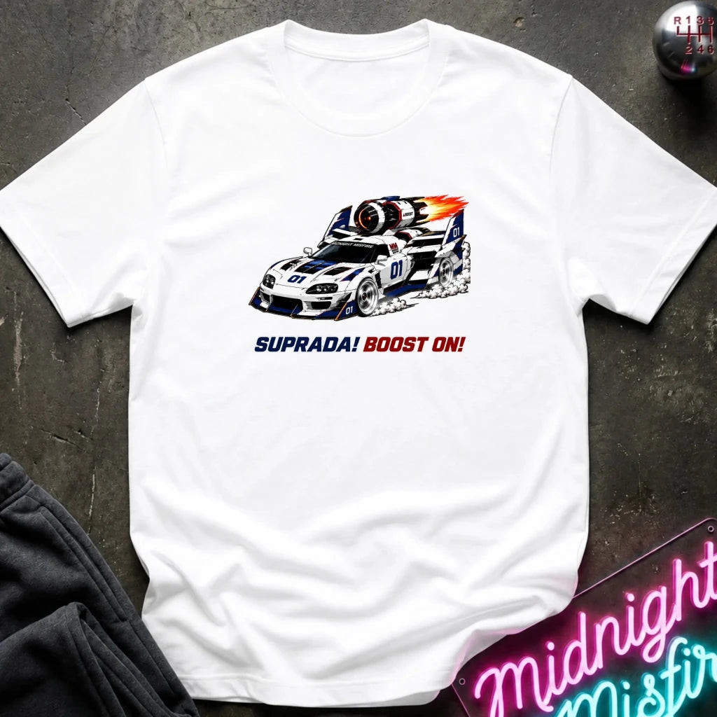 A white short-sleeve t-shirt laid flat on a dark textured surface, featuring a graphic of a white and blue race car with red and orange flames, and the text 'SUPRADA! BOOST ON!' printed below.