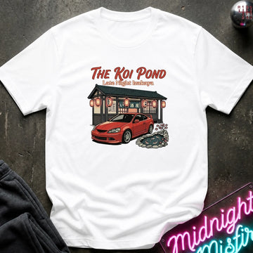 A white short-sleeve graphic t-shirt laid flat on a dark textured surface. The graphic features the text 'THE KOI POND Late Night Hamburger' above an illustration of a red sports car parked in front of a restaurant with red lanterns and a koi pond.