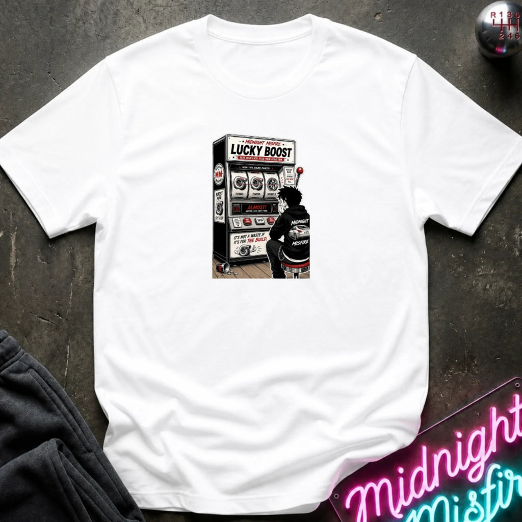 A white short-sleeve crewneck t-shirt laid flat on a dark textured surface, featuring a central graphic of a person sitting in front of a slot machine labeled 'LUCKY BOOST'.