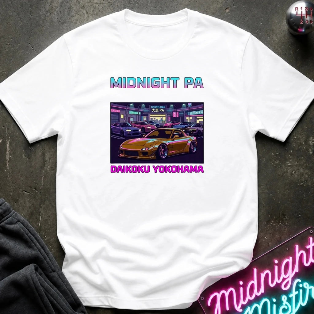 A white short-sleeve t-shirt laid flat on a dark textured surface, featuring a graphic print of a yellow sports car in a neon-lit parking lot with the text 'MIDNIGHT PA' above and 'DAIKKU YOKOHAMA' below.