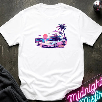 A white short-sleeve t-shirt laid flat on a dark textured surface, featuring a colorful retro graphic of a white sports car on a beach with palm trees and a sunset.