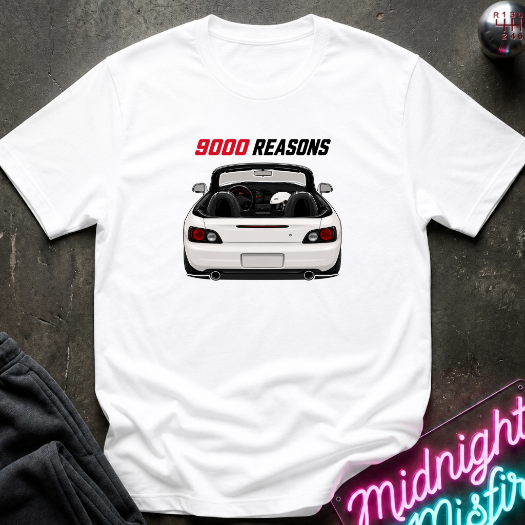 A white short-sleeve t-shirt laid flat on a dark textured surface, featuring a graphic of a white convertible sports car with the text '9000 REASONS' above it in red and black. A neon sign and dark pants are partially visible as props.