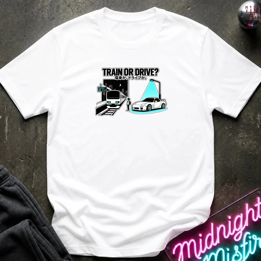 white graphic t-shirt laid flat on a dark textured surface. The graphic features a train and a car with a person.