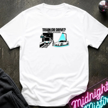 white graphic t-shirt laid flat on a dark textured surface. The graphic features a train and a car with a person.