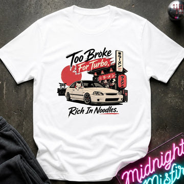 White short-sleeve graphic T-shirt laid flat on a dark textured surface. The shirt features a printed design of a white sports car in front of a Japanese-style street scene with a red sun and neon signs, plus the text 'Too Broke For Turbo' and 'Rich In Noodles.