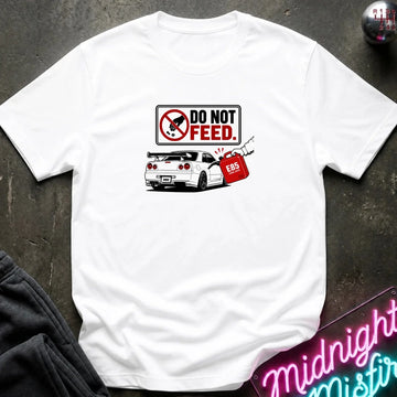 A white short-sleeve graphic t-shirt laid flat on a dark textured surface. The graphic features a 'DO NOT FEED' sign.