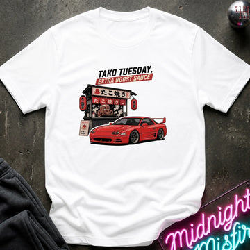 A white short-sleeve graphic T-shirt laid flat on a dark textured surface. The shirt features a red sports car and a Japanese street food stall graphic with the text 'TAKO TUESDAY.