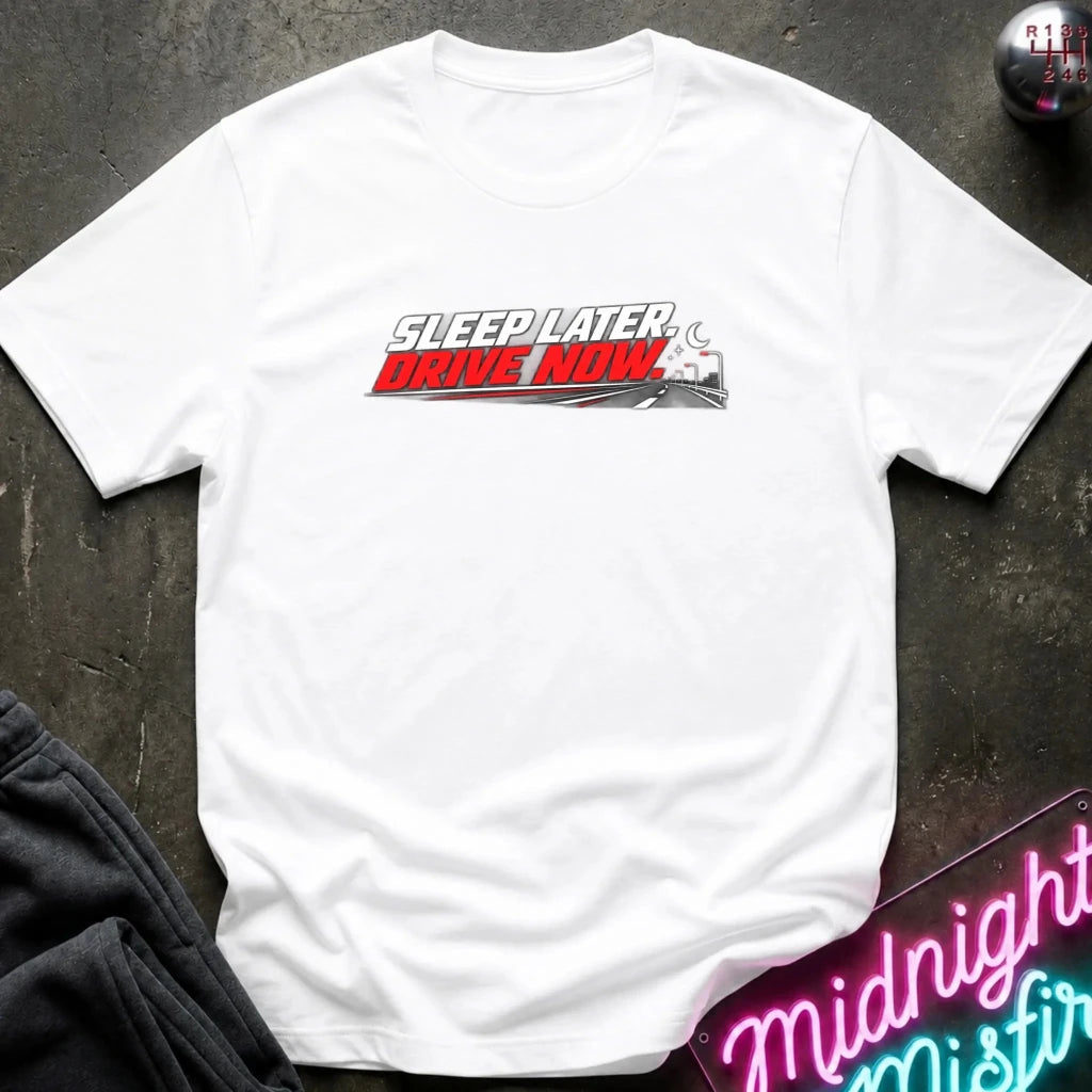 A white short-sleeve graphic T-shirt laid flat on a dark textured surface. The shirt features a central blueprint-style illustration of an engine with pastel blue and pink details and the text 'MIDNIGHT MISFIRE.