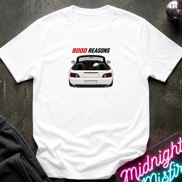 A white short-sleeve t-shirt laid flat on a dark textured surface, featuring a graphic of a white convertible sports car with the text '9000 REASONS' above it. A neon sign and dark clothing are partially visible in the background as styling props.