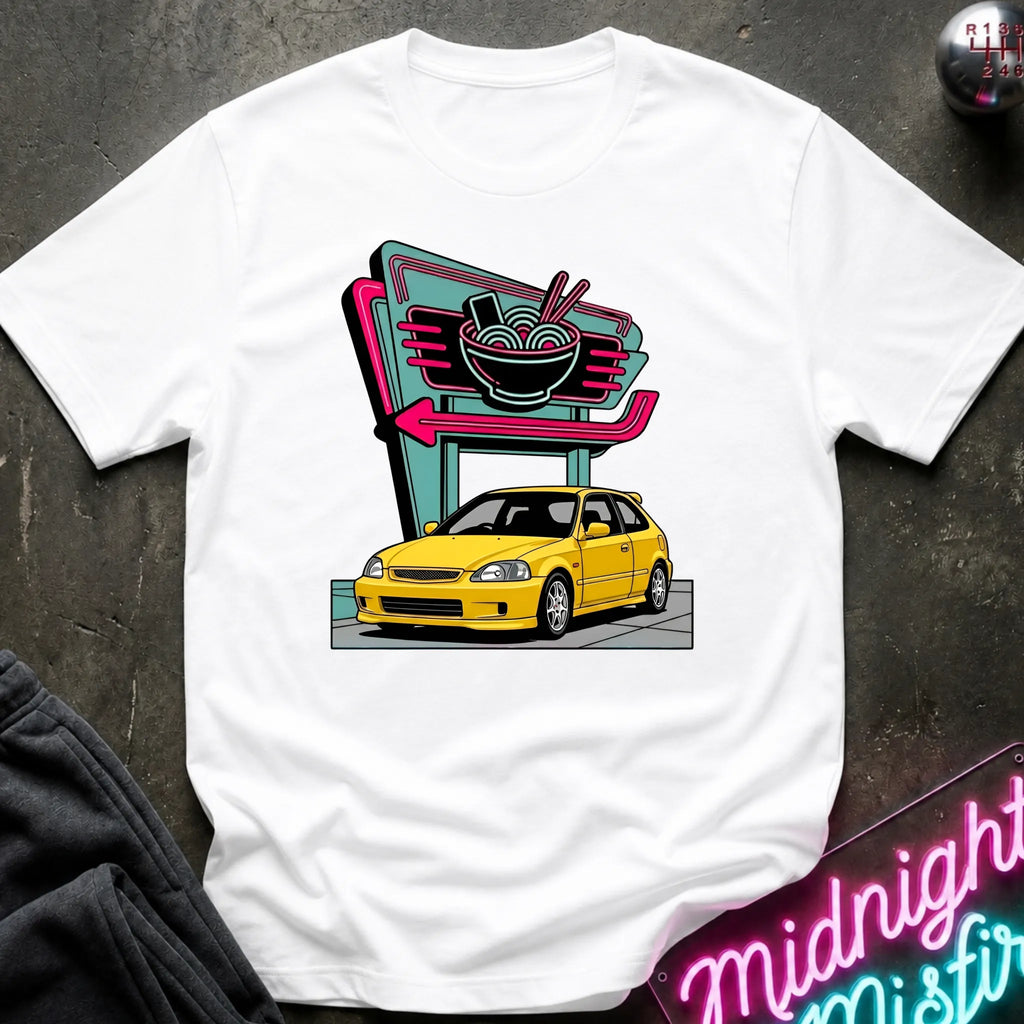 A white short-sleeve crewneck t-shirt laid flat on a dark textured surface, featuring a colorful graphic print of a yellow car parked in front of a retro neon ramen shop sign.
