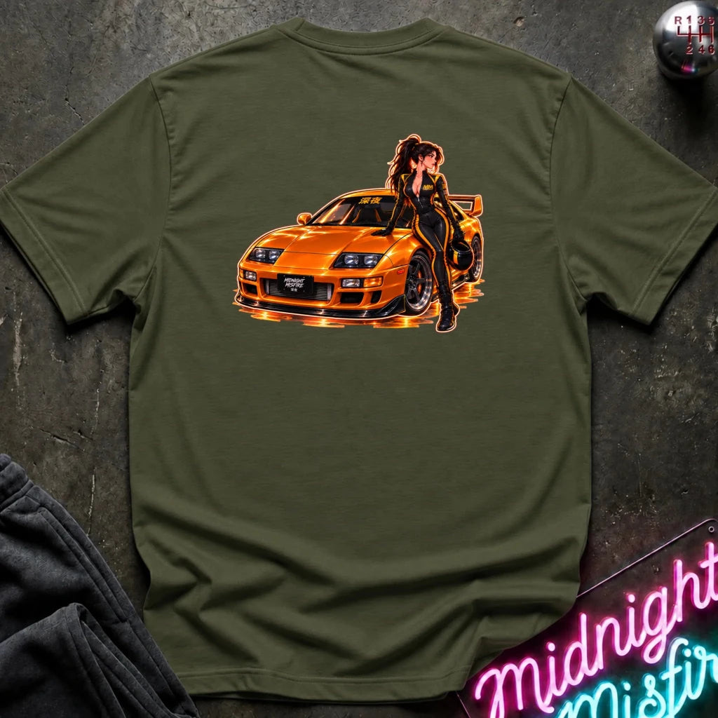 An olive green short-sleeve t-shirt laid flat on a dark textured surface, featuring a large graphic print of an orange sports car with a woman in a black outfit on the back.