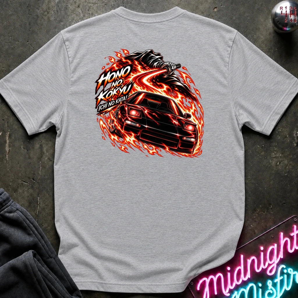 A light gray heather short-sleeve t-shirt laid flat on a dark textured surface, showing the back graphic with a car and the text "ichi no kata!"