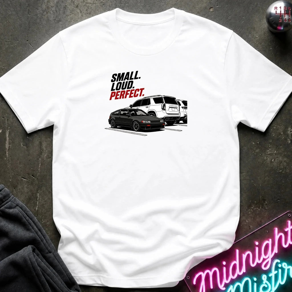 A white short-sleeve graphic t-shirt laid flat on a dark textured surface. The graphic features the text 'SMALL.