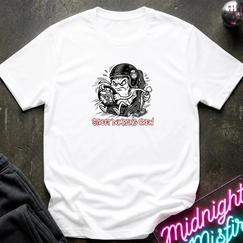 A white crewneck t-shirt laid flat on a dark textured surface. The shirt features a graphic of a street-dumper character wearing a helmet and goggles, with the text 'STREET DUMPING CREW' printed below in a pink font.
