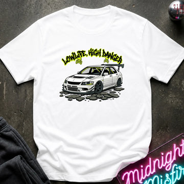 A white short-sleeve graphic T-shirt laid flat on a dark textured surface. The shirt features a printed illustration of a white sports car with the text 'LOW LIFE, HIGH DANGER' in yellow above it.