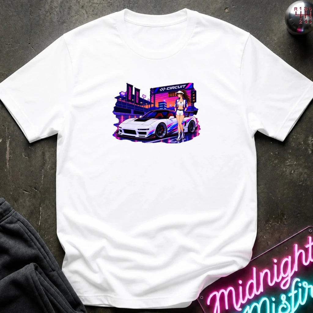 A white short-sleeve crewneck t-shirt laid flat on a dark textured surface, featuring a colorful graphic print of a white sports car in front of a neon-lit cityscape with a woman standing beside it.