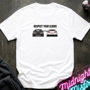 white graphic t-shirt laid flat on a dark textured surface. The graphic features the text and blue car facing a white car.