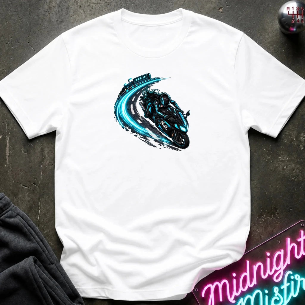 A white short-sleeve t-shirt laid flat on a dark textured surface, featuring a graphic print of a black motorcycle with a glowing blue trail effect. Styled flat-lay props include a pair of dark sweatpants in the lower-left corner and a neon sign in the lower-right corner.