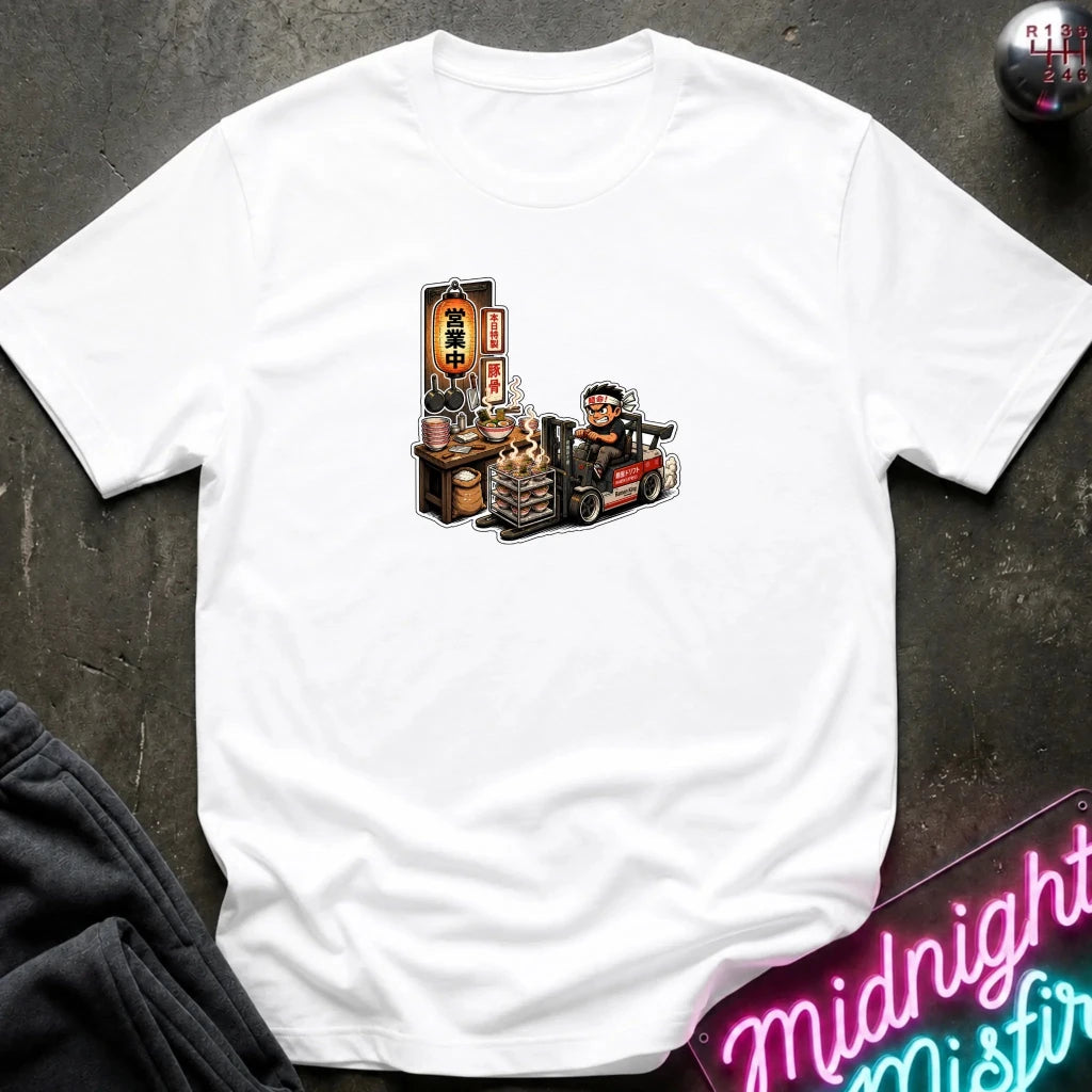 A  white short-sleeve t-shirt with a cartoon graphic of a street food vendor on a forklift, laid flat on a dark textured surface with a neon sign and folded sweatpants nearby.