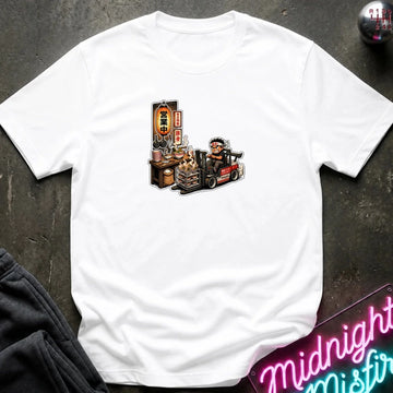 A  white short-sleeve t-shirt with a cartoon graphic of a street food vendor on a forklift, laid flat on a dark textured surface with a neon sign and folded sweatpants nearby.