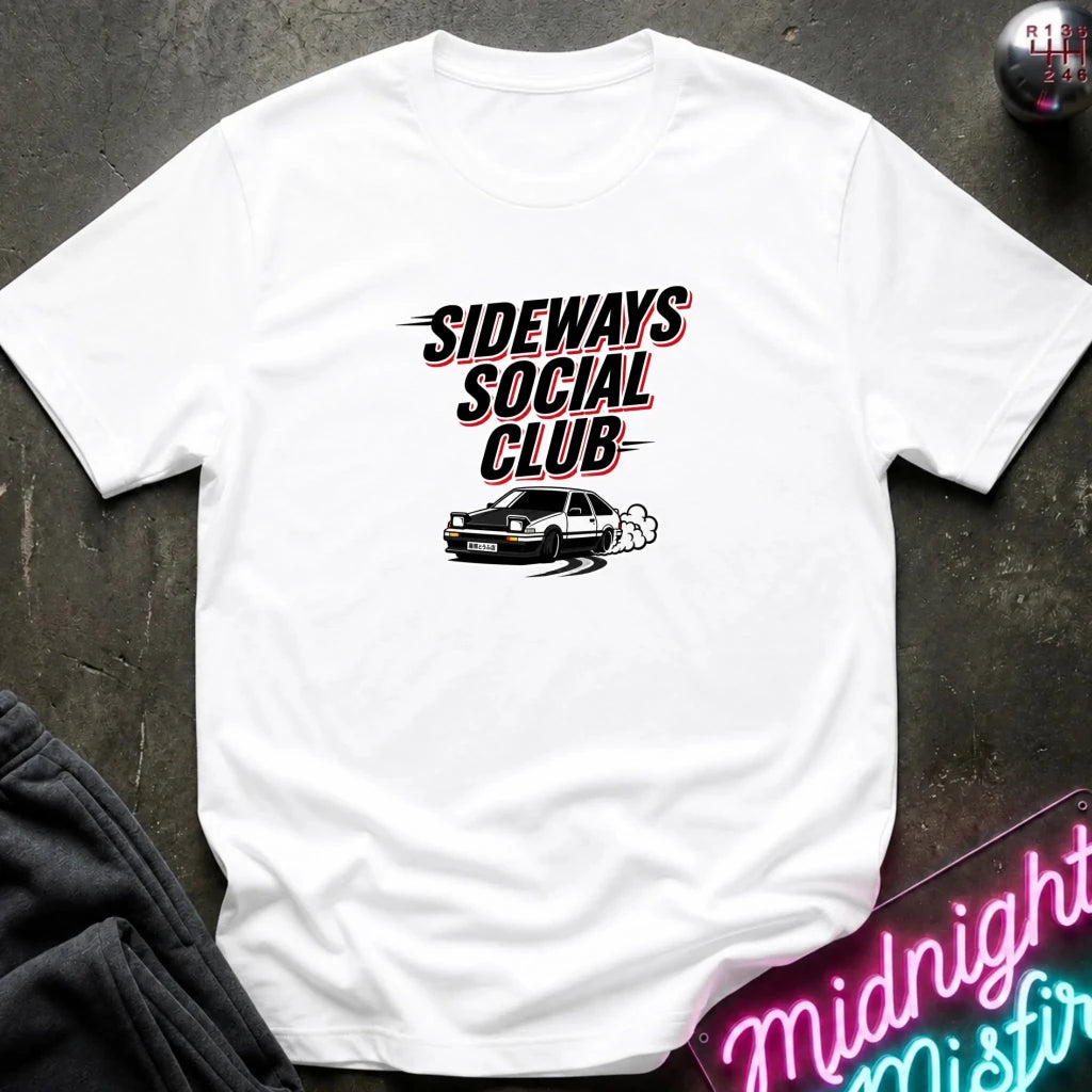 A white short-sleeve graphic t-shirt laid flat on a dark textured surface. The graphic featurestext above an illustration