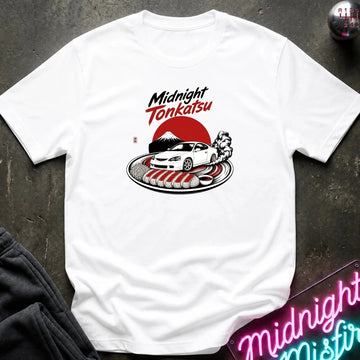 A white short-sleeve graphic t-shirt laid flat on a dark textured surface. The graphic features the text 'Midnight Tonkatsu' in black and red, above a white car, a red sun, and a Japanese dish on a plate.