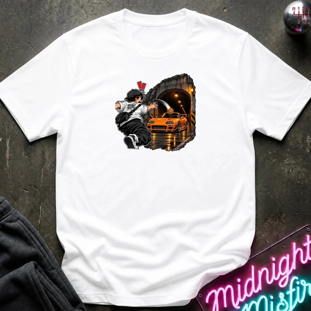 A white short-sleeve crewneck t-shirt laid flat on a dark textured surface. The center of the shirt features a graphic print of an anime character in a black and white outfit with a hat, next to a sports car 