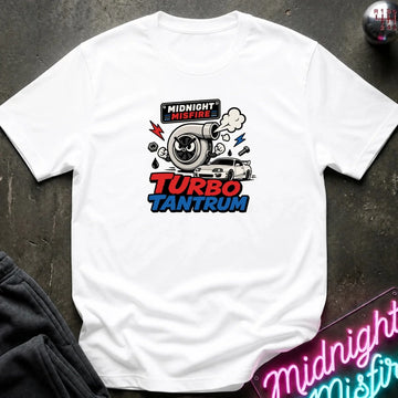 A white short-sleeve graphic t-shirt laid flat on a dark textured surface. The graphic features a turbocharger illustration with the text 'MIDNIGHT MISFIRE' above and 'TURBO TANTRUM' below in red and blue.