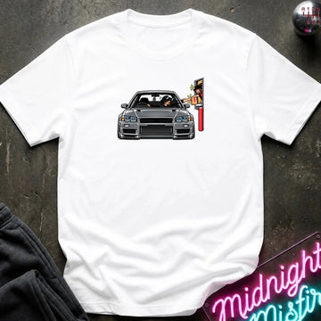 A white short-sleeve t-shirt laid flat on a dark textured surface, featuring a graphic print of a gray sports car with a driver and a red-and-yellow sign on the chest. 