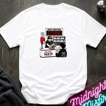 A white short-sleeve crewneck t-shirt featuring a retro-style graphic of a mechanic working at a parts counter with a digital display showing 'NOW SERVING: 0086'. 