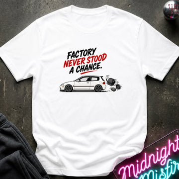 A white hort-sleeve graphic t-shirt laid flat on a dark textured surface. The graphic features the text 'FACTORY NEVER STOOD A CHANCE.
