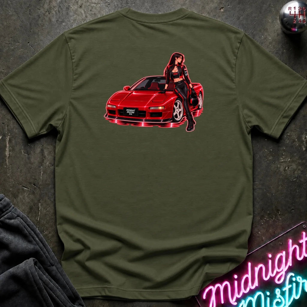 An olive green crewneck t-shirt laid flat on a dark textured surface, featuring a graphic print of a red sports car with a woman leaning on it. 