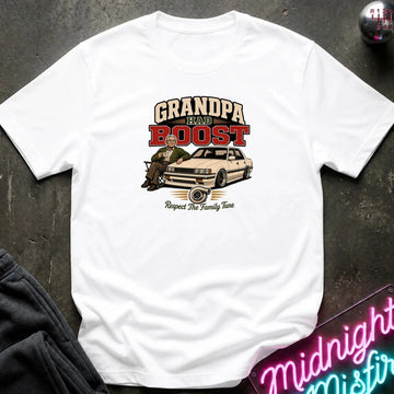 A white short-sleeve graphic t-shirt laid flat on a dark textured surface. The graphic features the text 'GRANDPA RAW BOOST' in beige and red, above an illustration of a man sitting in a car with the phrase 'Respect The Family Tune' below.